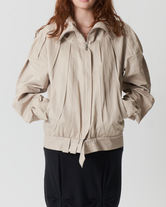 Person wearing a beige jacket and black pants on a white background