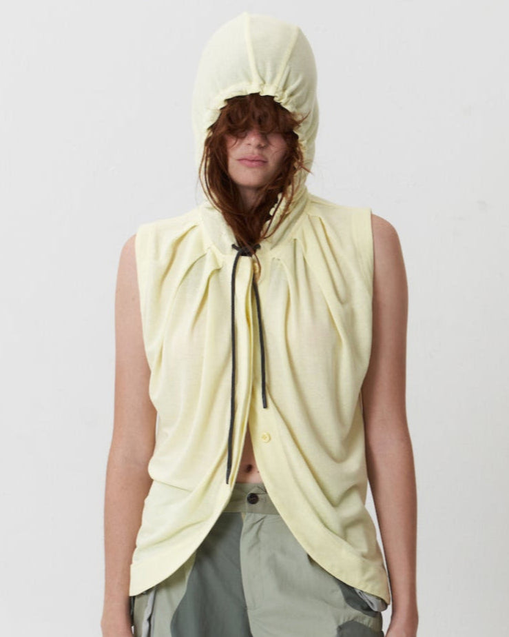 A sleeveless hooded button-down top in a beige color, with pleated shoulders and a keyhole button placket at the front.