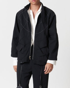 A person wearing a silver zipper pocket jacket with woven fabric panels, featuring white topstitching over the shoulders.