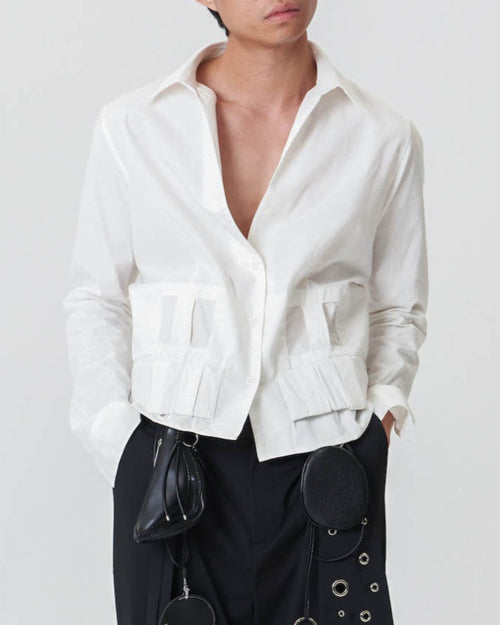 A person wearing a white button-down shirt with V-neckline, two rows of belt loops, and an elastic hem, paired with black pants.